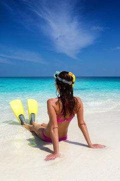 Attraktive Frau mit Schwimmflossen und Taucherbrille sitzt am tropischen Strand und genießt ihren Urlaub