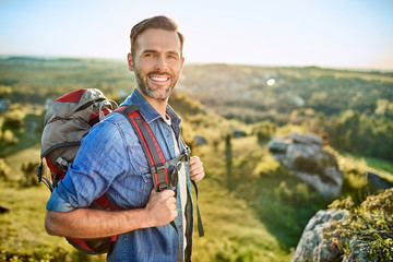 Portrait of cheerful man with backpack during hiking trip in the mountains - obrazy, fototapety, plakaty