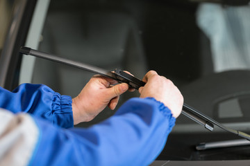 Technician is changing windscreen wipers on a car station. - obrazy, fototapety, plakaty
