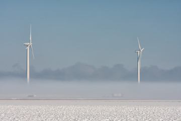 Dutch winter landscape with highway covered in ground fog and wind turbines against a blue sky