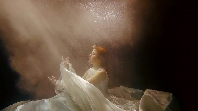 a sea nymph is under water, a lady with red hair is looking up at the light