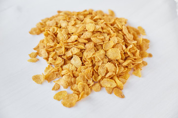 Heap of cornflakes on a painted white wooden background. Cornflakes scattered on a wooden table.