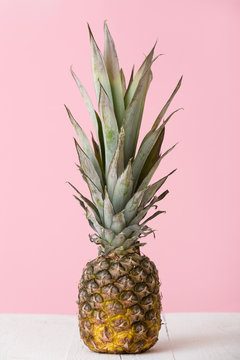 View on fresh organic pineapple on light pink background and on white wooden table. Healthy food.
