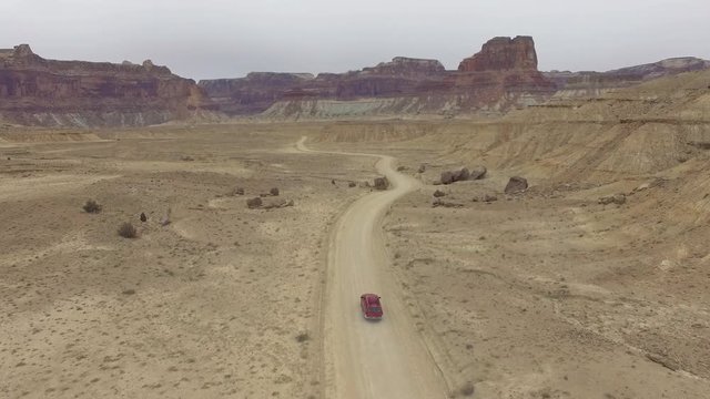 Aerial view following truck driving on dirt road through the Utah desert in the San Rafael Swell.