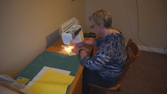 Mature woman sewing a quilting square to craft a homemade quilt or blanket