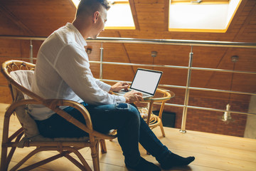 Side view shot of man sitting at home and working on laptop. Caucasian male working from loft home...