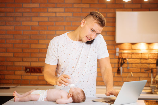 Dad Trying To Work, Cooking And Talk On Phone While Standing With His Newborn Babe In Home Office Interior