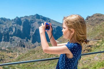 Mädchen mit zerzaustem Haar fotografiert eine bergige Landschaft bei Sonnenschein