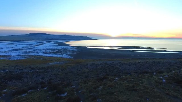 Aerial view of a beach with the sunset on the horizon and some sonw on the beach sand