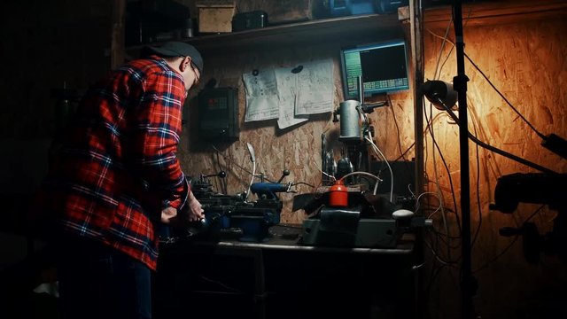 male master working on an old lathe machine in a dark workshop garage