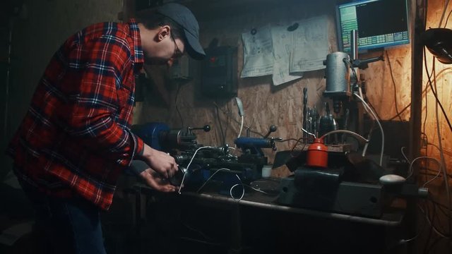 male master working on old lathe machine processing metal flying sparks in a dark workshop garage