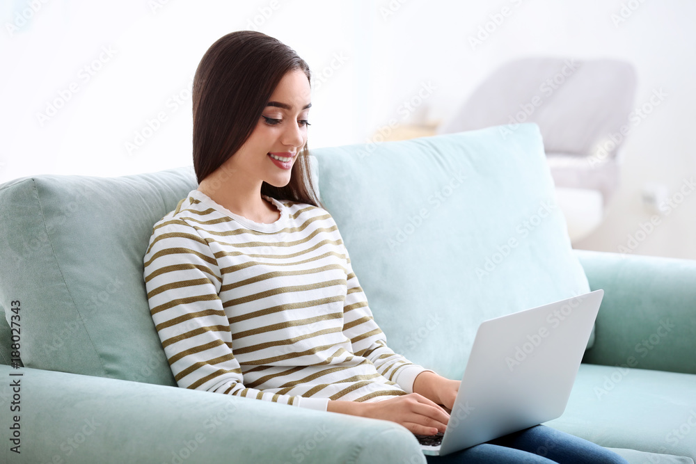 Canvas Prints Young woman with modern laptop sitting on sofa at home