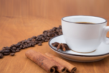 Coffee cup and beans, cinnamon sticks, on wooden table on background