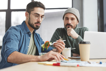 Crew of creative business worker discuss information during training workshop. Professional male vegeterian has snack at work while explains his new strategy to colleague, has attentive look