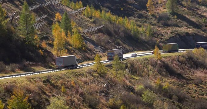 Trucks on a mountain road, Cinema 4k handheld pan view following trucks on a fall color road, in a alpine valley, on the top of simplon pass, on a sunny day, in Valais, Switzerland