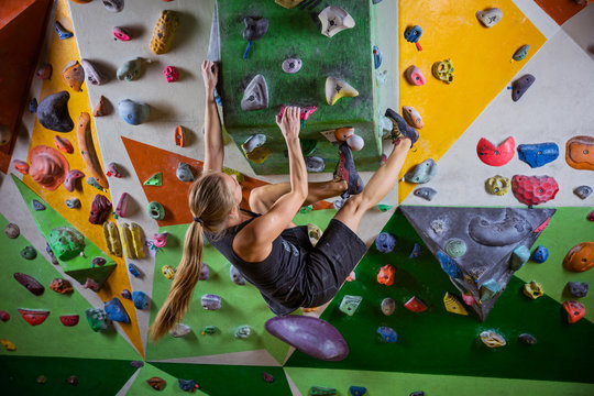 Young woman bouldering on overhanging wall in climbing gym