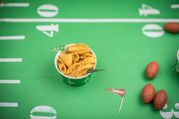 closeup of paper bowl of corn chips on green field with yard lines for big game