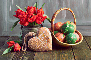 Easter composition with red tulips, wooden heart and a basket of colored Easter eggs on wood