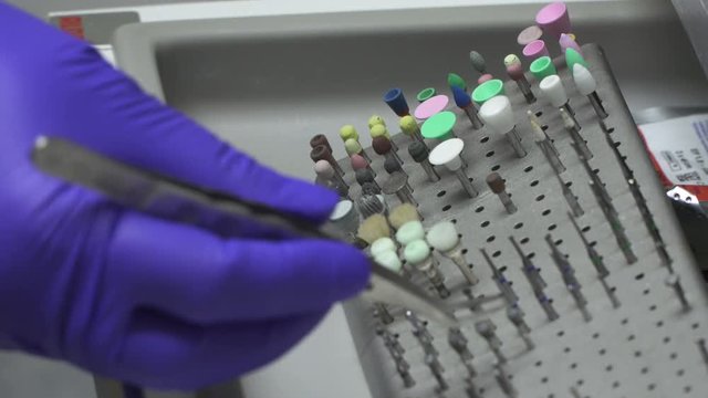 Close-Up Of Dentist's hand in gloves selecting a bur from set in a shelf .Dentist Equipment - Dental Care.