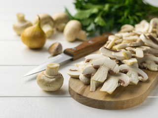 Fresh sliced mushrooms on chopping Board and onion and herbs on white wooden table.