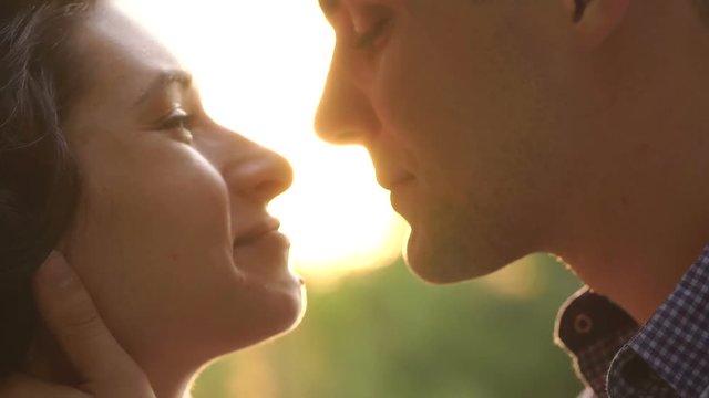 Close-up of a young attractive couple is kissing at sunset. Close-up portrait of young kissing couple at sunshine. Slow motion. Silhouette.