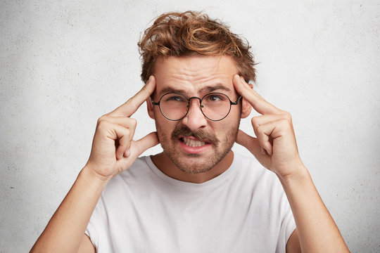 Handsome male tries to concentrate and remember some details, keeps finger on temples and clenches teeth, frowns face with dissatisfaction as being forgetful and absent minded. Hmm let me think