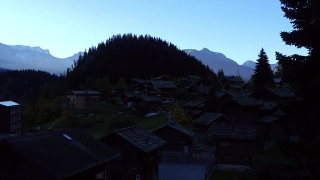 BLATTEN, VALLIS, SWITZERLAND, OCTOBER 15 UHD zoom out time lapse view of sun revealing a mountain alpine town, on a sunny autumn morning dusk, in Blatten bei naters, Vallis, Switzerland