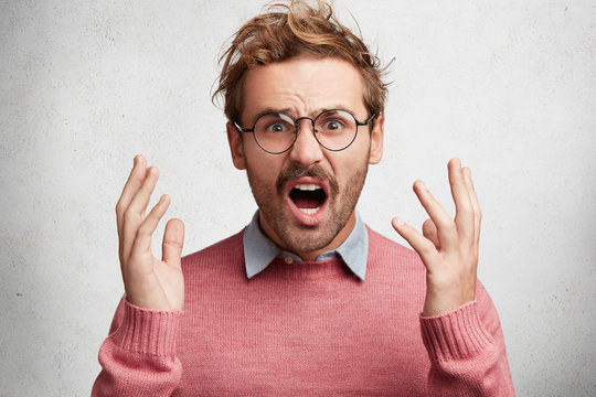 Disturbed displeased man gestures angrily, has irritated expression, can`t recieve critic on his side, exclaims in despair. Young male has quarrel with someone, tries to prove his rightness.