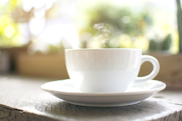 Close up a steaming white cup of hot cappuccino with bokeh tree background