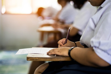 Close up hand of fat student reading and writing exam with stress in classroom.