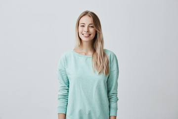 European female model with long blonde hair, wears light blue sweater, looks at camera with...