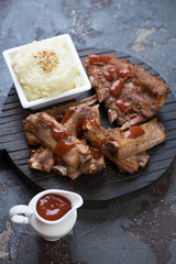 Baked pork ribs with potato puree and sauce on a wooden chopping board, selective focus, studio shot