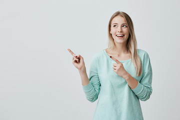 Happy surprised blonde young female smiling broadly at camera, pointing fingers away, showing...