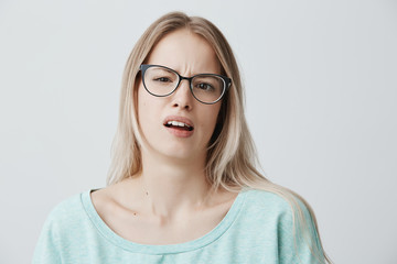 Fototapeta premium Attractive european female with slanting eyes and blonde long hair has upset look, being abused by someone, expresses dissatifaction and discontent, frowns face. Negative emotions and feelings.