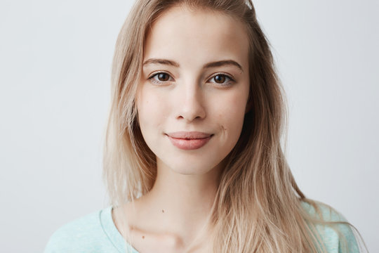 Beautiful female having dark shining eyes, pure skin and blonde straight hair wearing loose sweater looking directly at camera having mysterious and glad expression. Face expressions and emotions