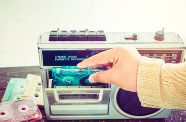 Retro lifestyle - Woman hand holding tape cassette with cassette player and recorder for listen music - vintage color tone effect.