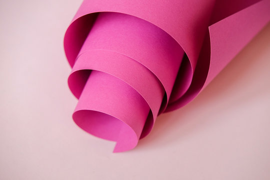 Pink paper folded into a tube on a light background. Monochrome designer paper.