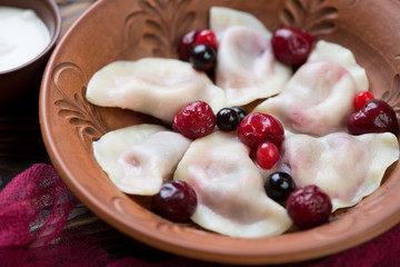 Close-up of boiled vareniki or dumplings with cherry stuffing served in a clay plate, selective focus