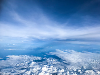 Aerial view among the sea of white clouds and deep blue sea with the blue sky from the seat of passenger in Airplane during the journey