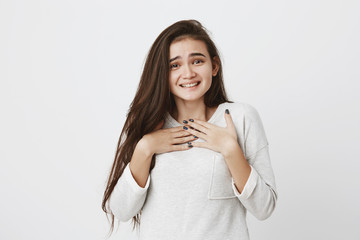 Shy cute teenage girl with long dark straight hair smiling cheerfully, demonstrating her white teeth, in casual clothes, pleased with present. Positive emotions, feelings and face expressions