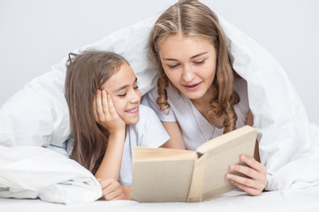 Fototapeta premium sisters reads a book on the bed under the blanket