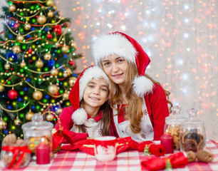Mom and daughter in Christmas hats sitting at a festive table