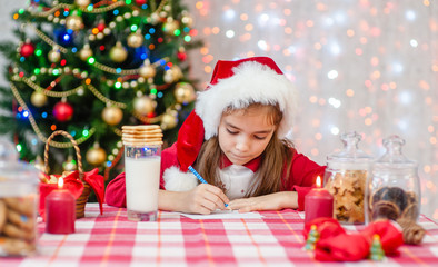 Little girl in red christmas hat writes letter to Santa Claus
