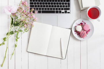 Feminine flat lay workspace with laptop, cup of tea, macarons and flowers, planner and pen on white...