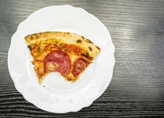 A bitten portion of pepperoni pizza on a plate. View from above.