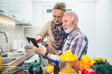 Senior couple using digital tablet in the kitchen at home for online shopping