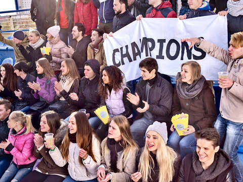 Fans cheering in stadium holding champion banner and singing on tribunes. Soccer game. People holding banner with Champion banner happily eating popcorn.
