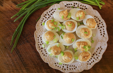 Deviled eggs with cod livers with leek on white plate. Rustic wooden table