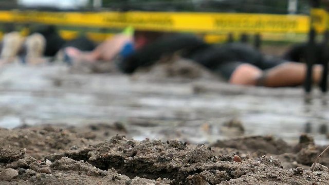 Competitors Crawling In Mud Under Barbed Wire In Obstacle Endurance Race