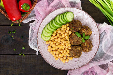 Tasty meat cutlets, chickpeas, fresh cucumber on a ceramic plate on a dark wooden background. The top view